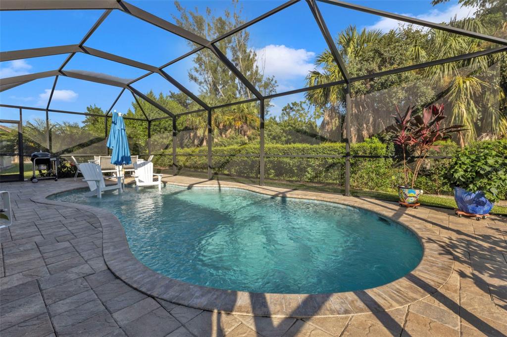 A screened-in pool area with a patio, lounge chairs, and lush landscaping in the background — 7676 MIKASA DRIVE, PUNTA GORDA, FL