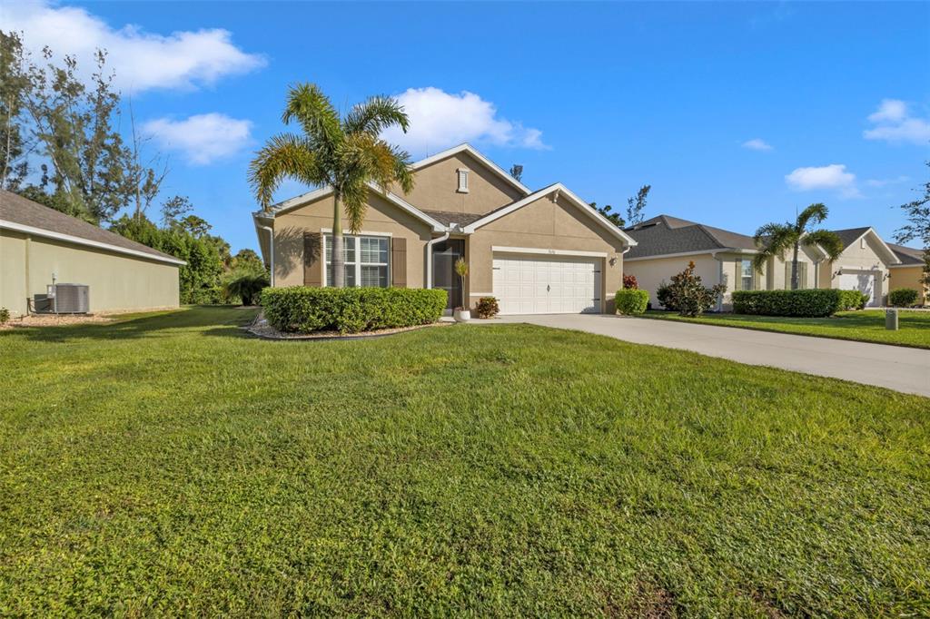 A single-story tan house with a two-car garage and a palm tree in the front — 7676 MIKASA DRIVE, PUNTA GORDA, FL