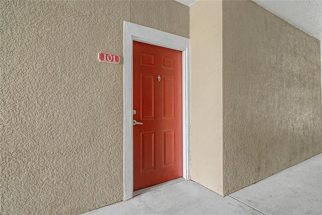 A red front door with the number 101 is set into a textured beige exterior wall — 8225 CLAIRE ANN DRIVE UNIT 101, ORLANDO, FL