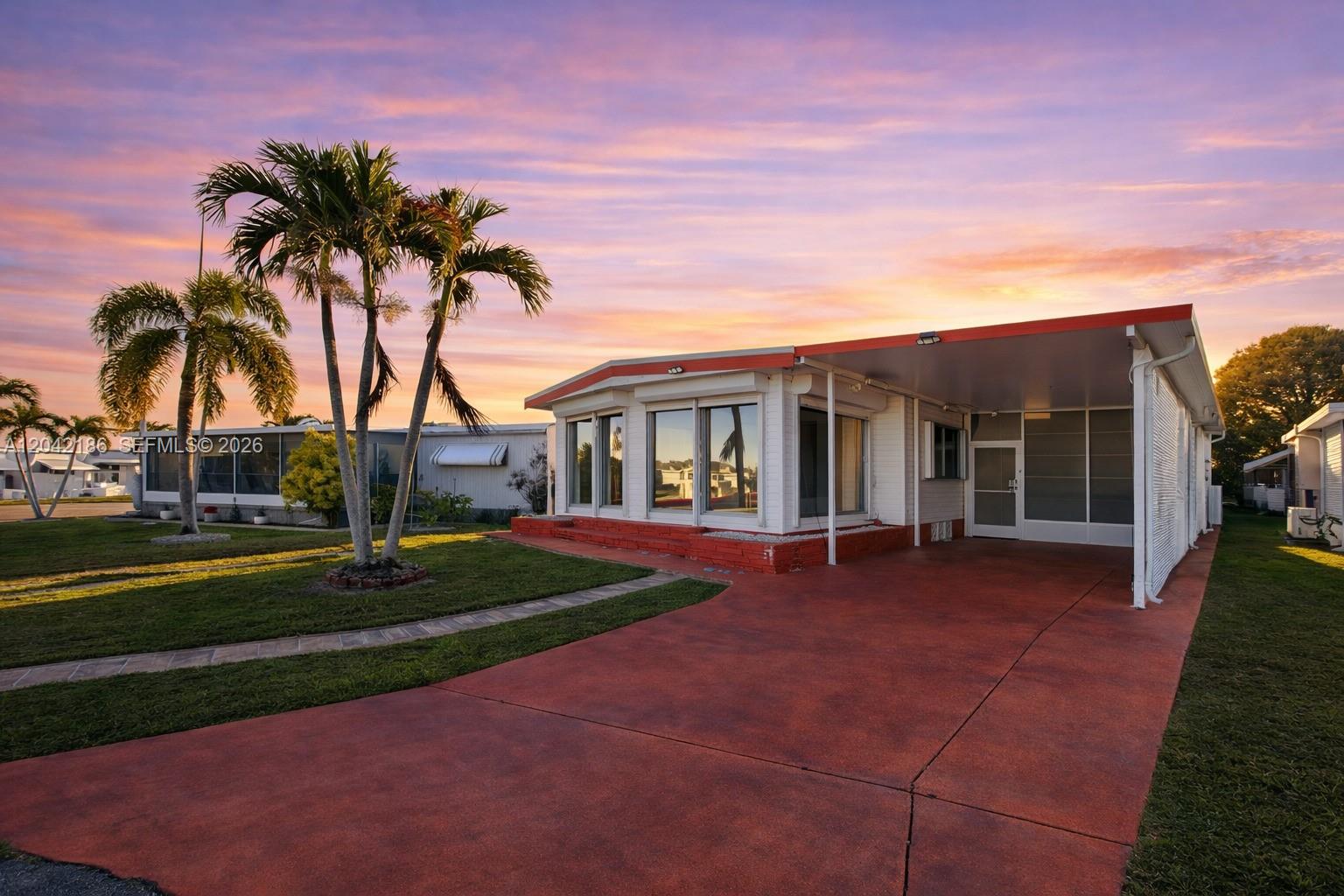 A single-story mobile home with a red driveway, carport, and palm trees at sunset — 2260 SW 85th Way, Davie FL 33324, DAVIE, FL