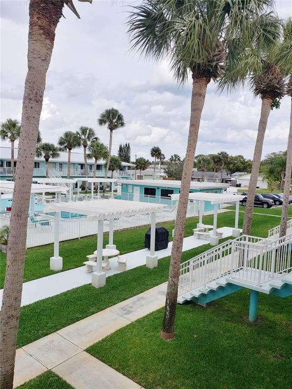 An outdoor courtyard features palm trees, white pergolas, a swimming pool, and a small building — 541 S PENINSULA AVENUE UNIT A21, NEW SMYRNA BEACH, FL