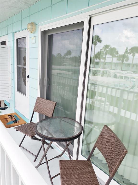 A balcony features a small glass-topped table and two wicker chairs outside sliding glass doors — 541 S PENINSULA AVENUE UNIT A21, NEW SMYRNA BEACH, FL