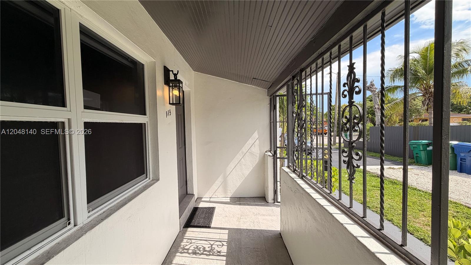 A covered porch features tiled flooring, a dark ceiling, and decorative metal security bars — 115 NW 118th St # 115, Miami FL 33168, MIAMI, FL