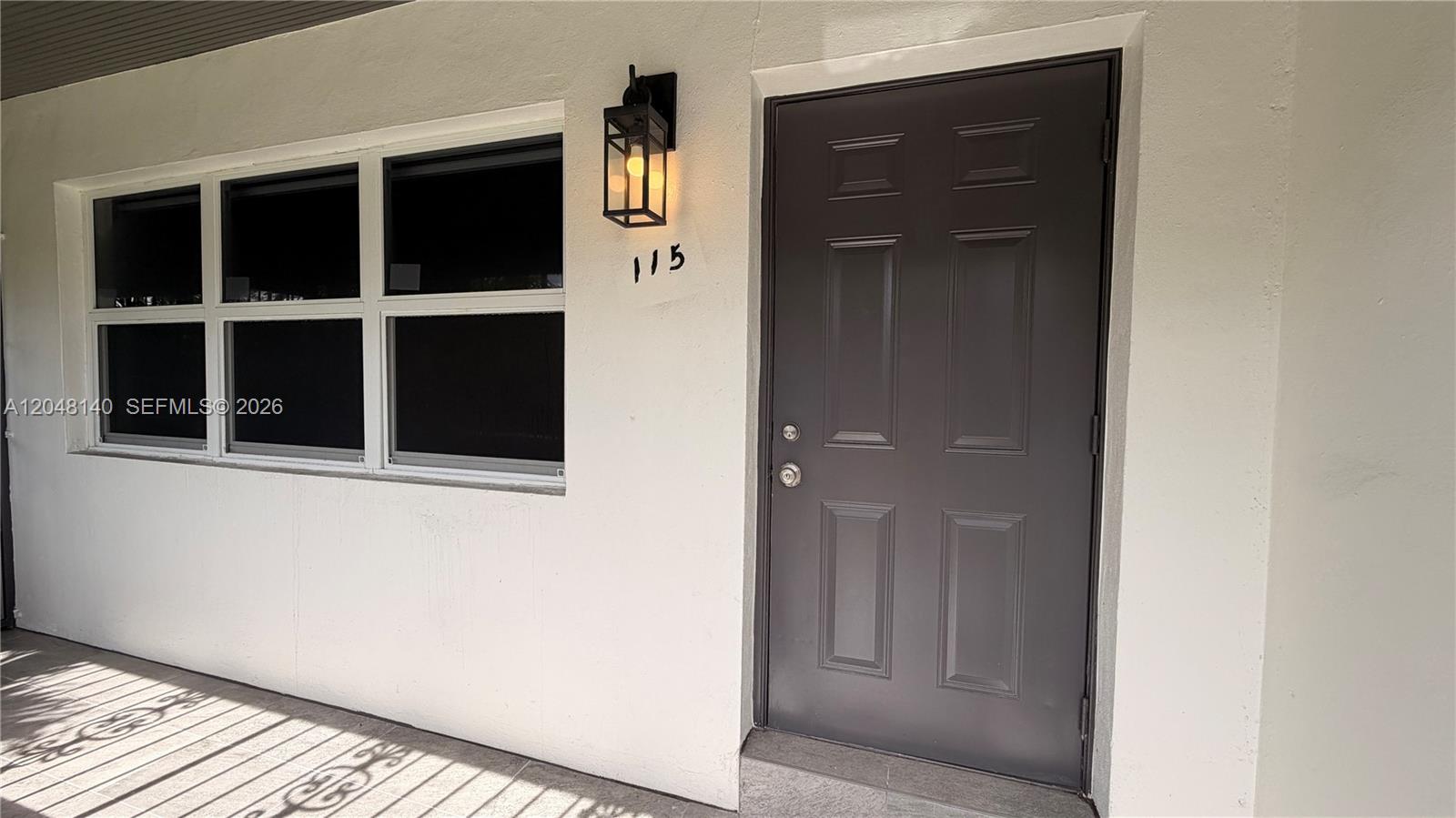 A dark gray door with a house number and a wall-mounted light fixture — 115 NW 118th St # 115, Miami FL 33168, MIAMI, FL
