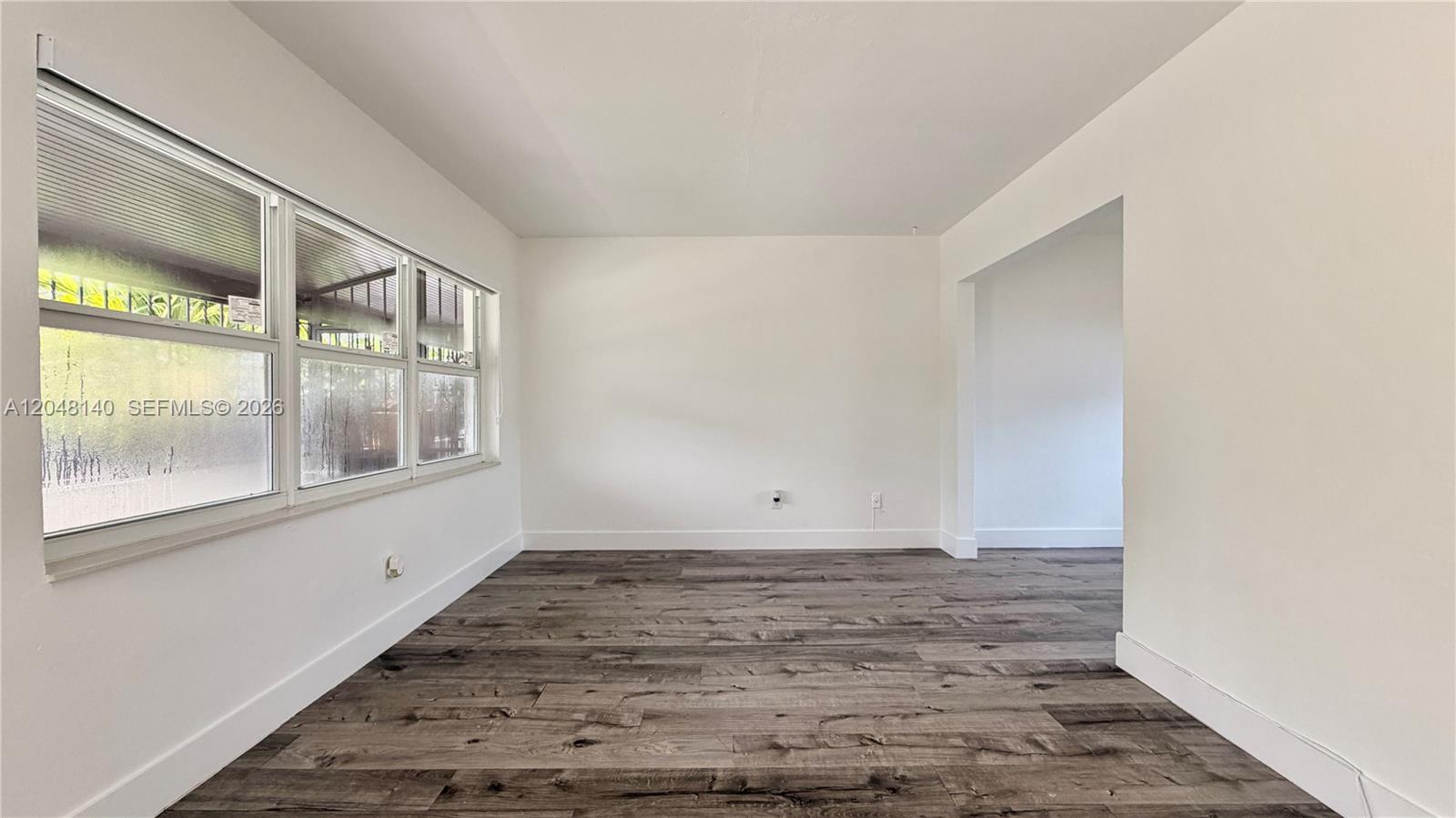 An empty room features white walls, gray wood-look flooring, and large windows — 115 NW 118th St # 115, Miami FL 33168, MIAMI, FL