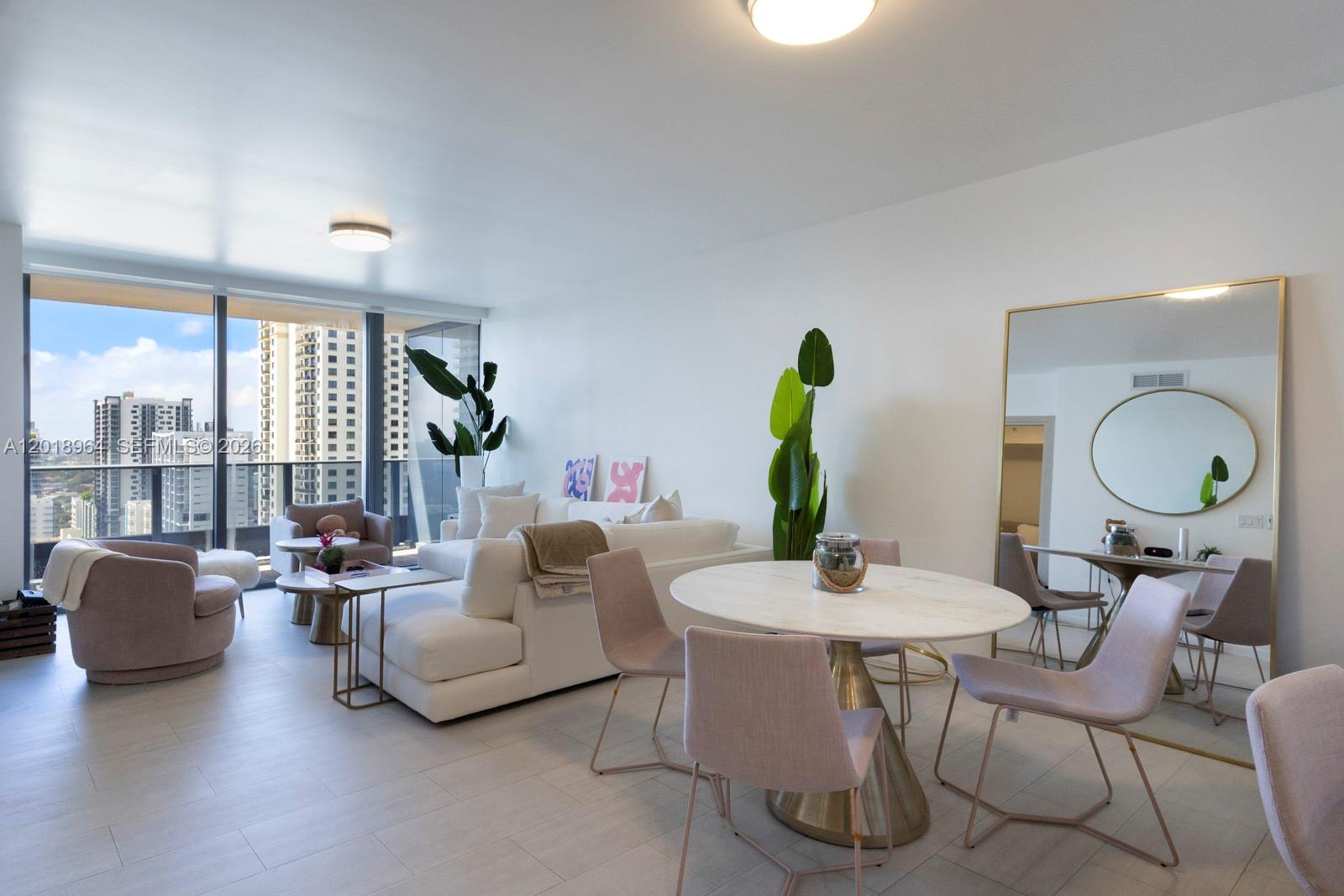 A bright living and dining area features white furniture, a round table, and city views — 1000 Brickell Plz # 2411, Miami FL 33131, MIAMI, FL