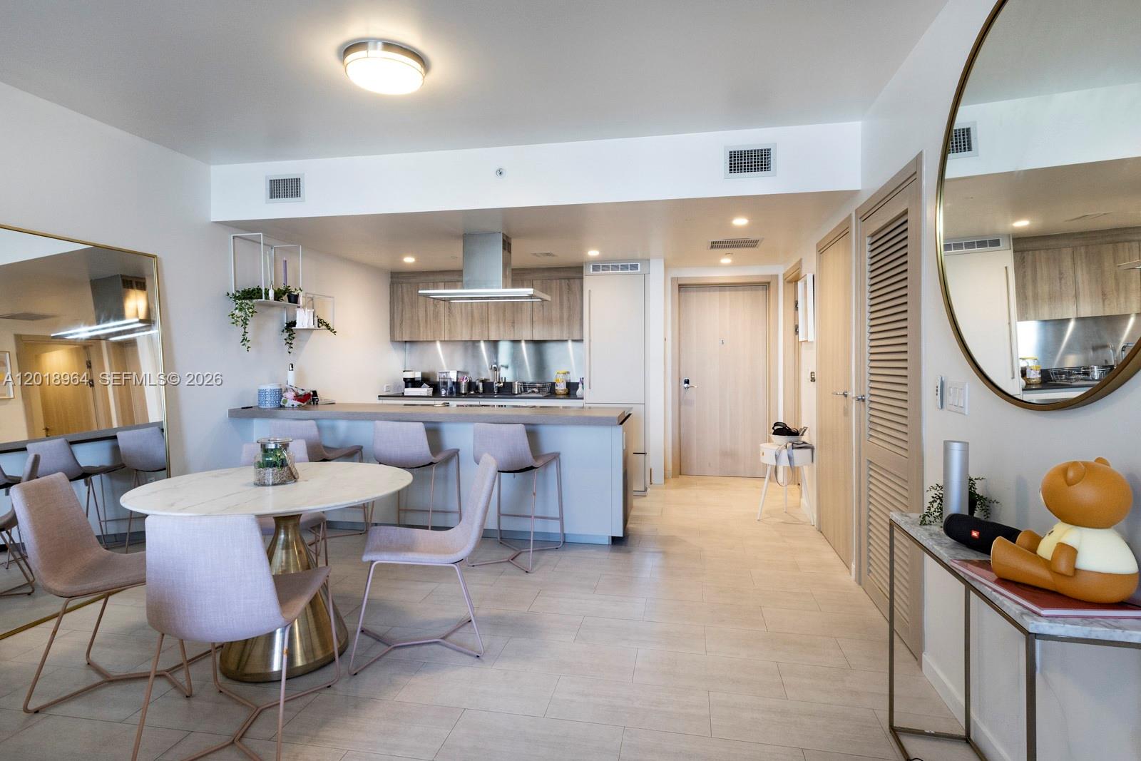 This open-concept kitchen and dining area features light wood cabinetry, bar seating, and tile flooring — 1000 Brickell Plz # 2411, Miami FL 33131, MIAMI, FL