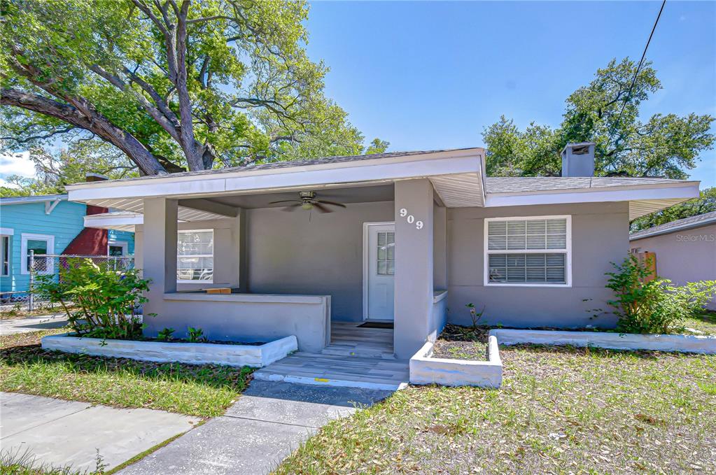 A single-story gray house features a covered front porch, a white door, and large trees — 909 HART STREET, CLEARWATER, FL