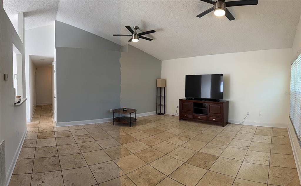 A living room with tile flooring, two ceiling fans, and a partially painted gray wall — 1432 DEW BLOOM ROAD, VALRICO, FL