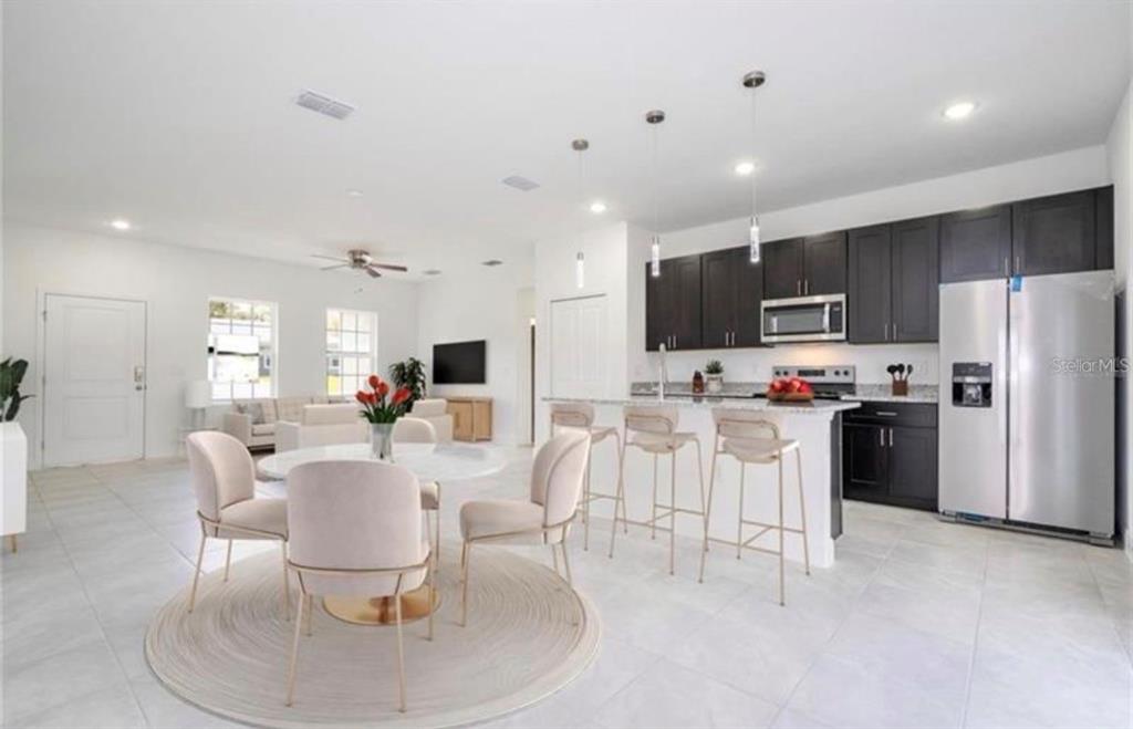 An open-concept kitchen and dining area features dark cabinetry, stainless steel appliances, and light tile — 9809 N SWANEE TERRACE, DUNNELLON, FL
