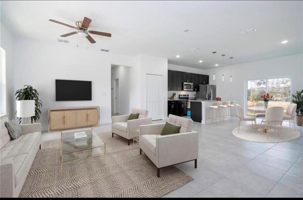 An open-concept living room and kitchen featuring light tile floors and modern neutral furniture — 9809 N SWANEE TERRACE, DUNNELLON, FL