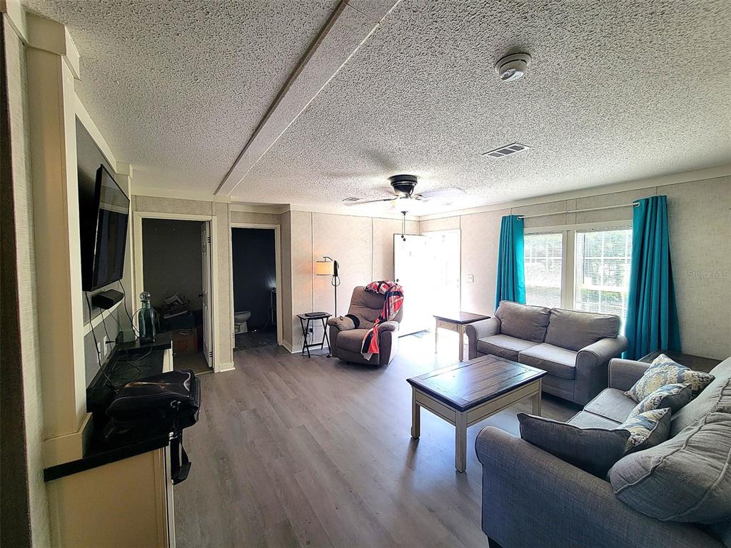 A living room features gray wood-look flooring, a ceiling fan, and two gray sofas — 2231 SE STATE ROAD 121, MORRISTON, FL