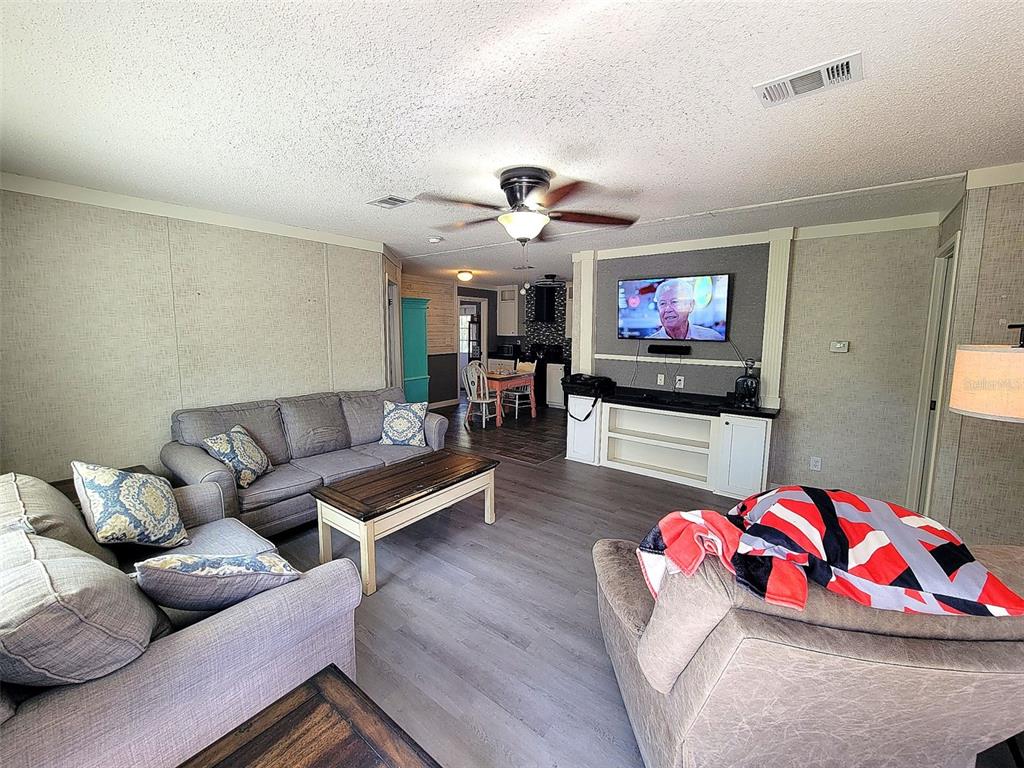 A living room features gray flooring, a ceiling fan, and a wall-mounted television — 2231 SE STATE ROAD 121, MORRISTON, FL