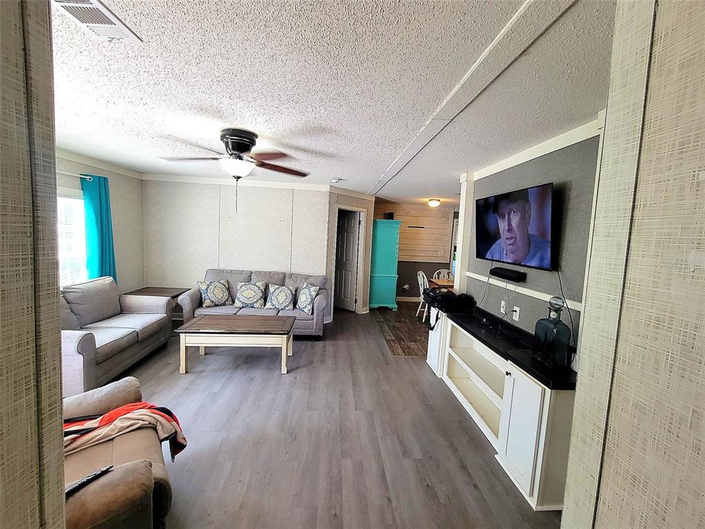 A living room features gray wood-look flooring, a gray sofa, and a wall-mounted television — 2231 SE STATE ROAD 121, MORRISTON, FL