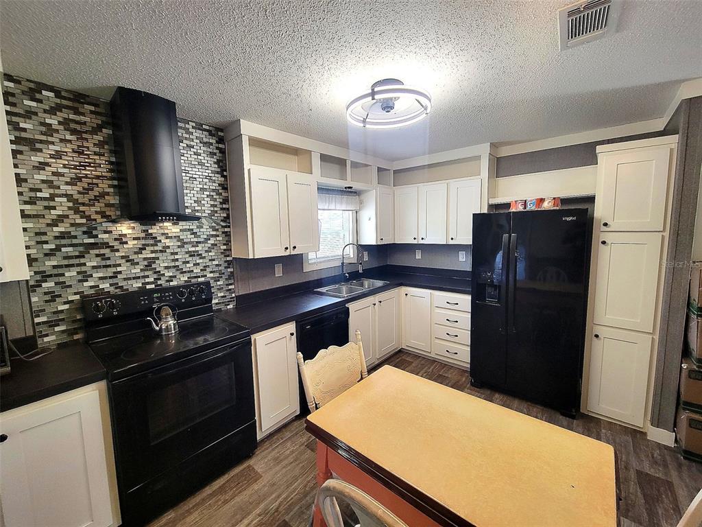 A kitchen features white cabinets, black appliances, a tiled backsplash, and a central dining table — 2231 SE STATE ROAD 121, MORRISTON, FL