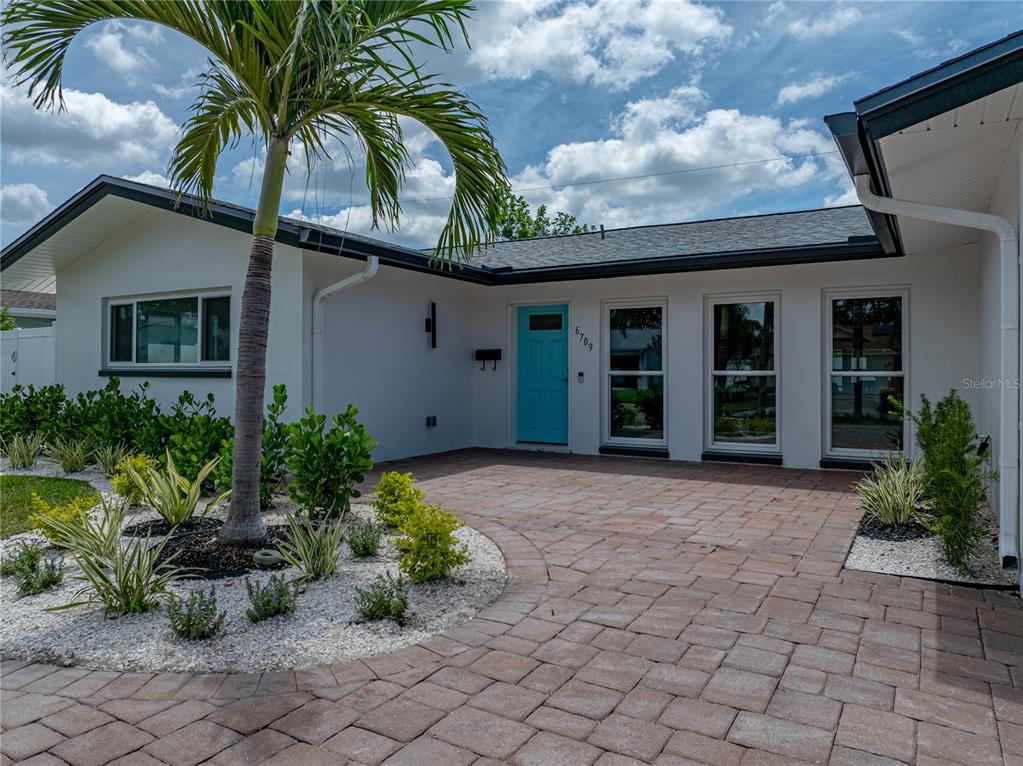 A white house with a blue front door and a paved driveway features a palm tree — 6709 CARDINAL DRIVE S, ST PETERSBURG, FL