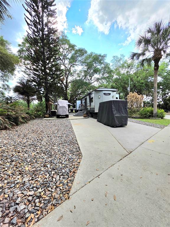 A recreational vehicle is parked on a concrete driveway next to a gravel yard — 159 HORSESHOE BEND, LAKE WALES, FL