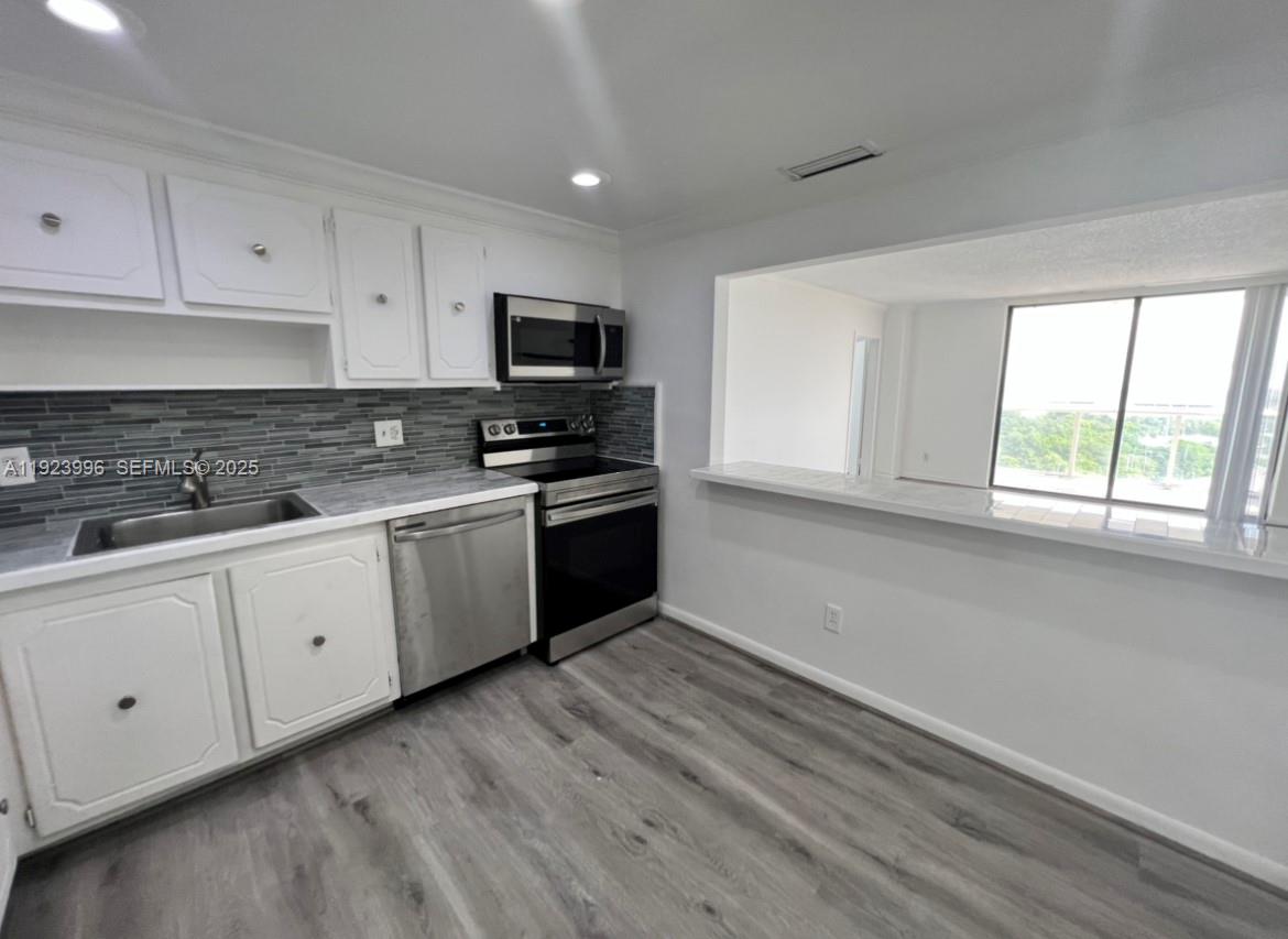 A kitchen with white cabinets, stainless steel appliances, gray tile backsplash, and a breakfast bar — 13499 Biscayne Blvd # 1205, North Miami FL 33181, NORTH MIAMI, FL