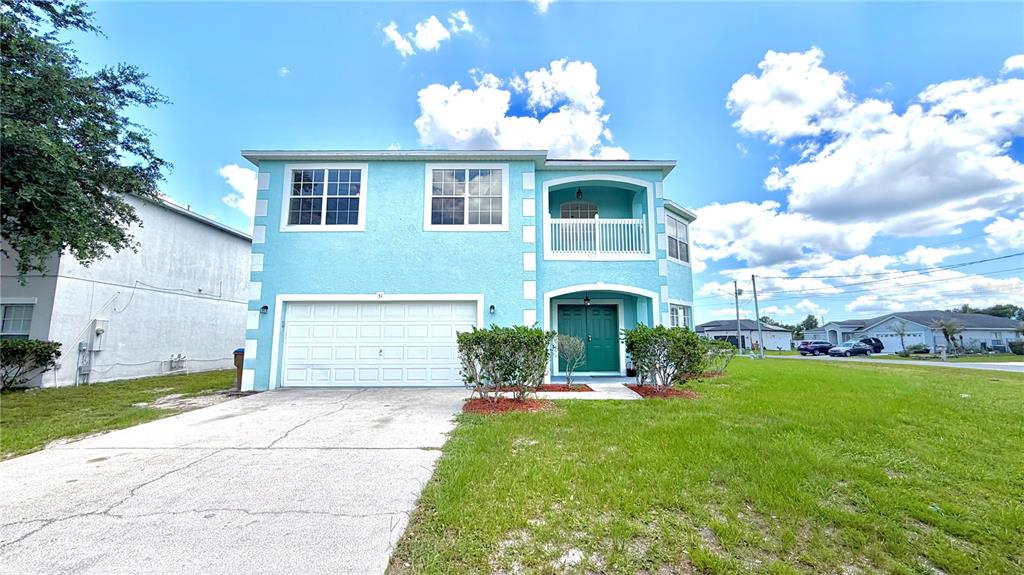 A two-story, light blue stucco house features a white garage door and a balcony — 51 ANDORA COURT, KISSIMMEE, FL