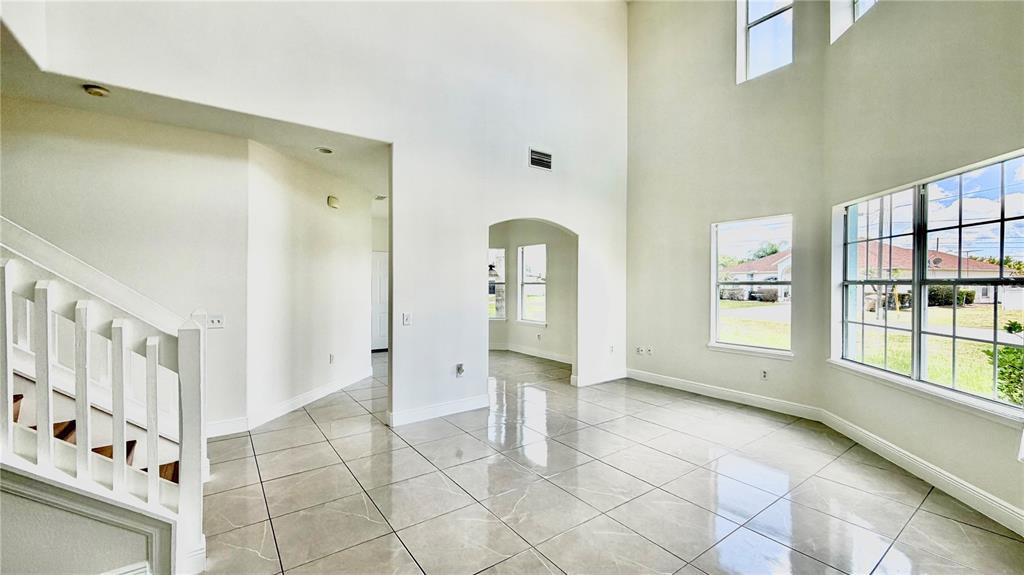 A bright, high-ceilinged living room features white walls, large windows, and light-colored tile flooring — 51 ANDORA COURT, KISSIMMEE, FL