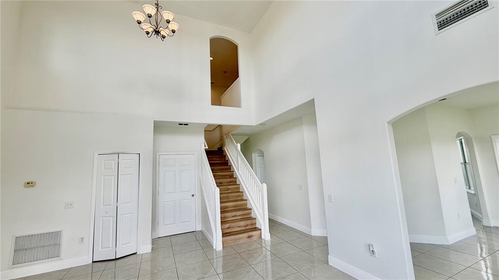 A high-ceilinged foyer features a wooden staircase, white walls, and light-colored tile flooring — 51 ANDORA COURT, KISSIMMEE, FL