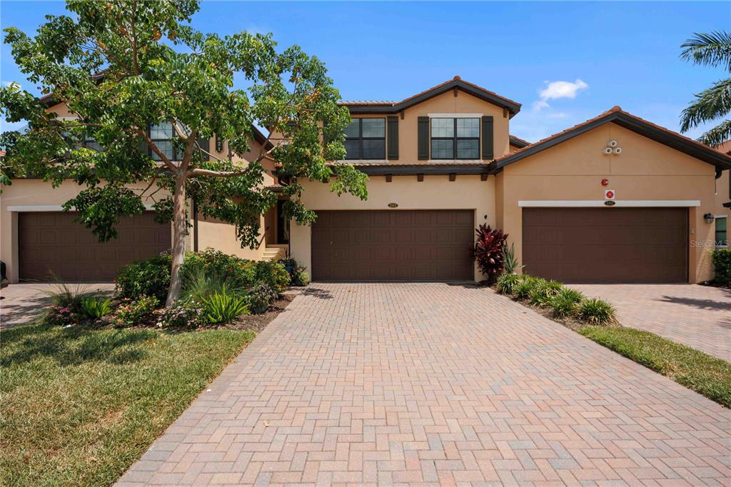 A two-story house with a three-car garage and a paved driveway under a blue sky — 10821 TARFLOWER DRIVE UNIT 202, VENICE, FL