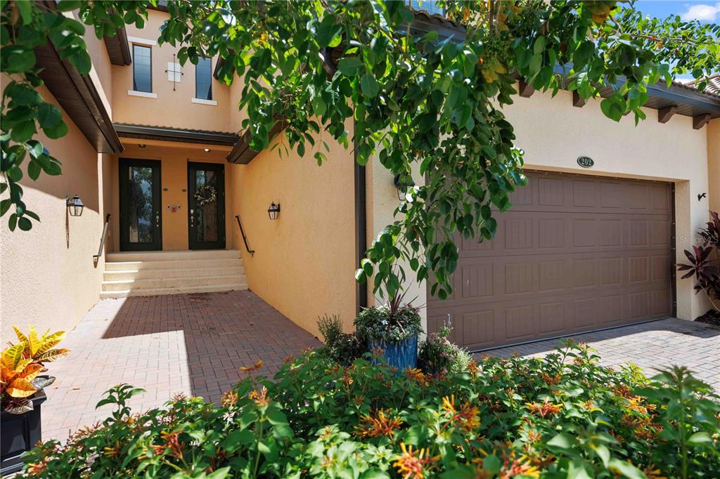 A tan stucco house exterior features a paved walkway, double front doors, and a garage — 10821 TARFLOWER DRIVE UNIT 202, VENICE, FL
