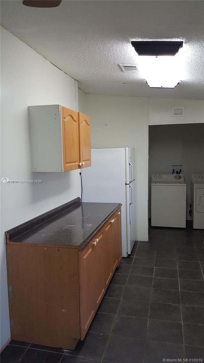 A kitchen with wooden cabinets, a dark countertop, a white refrigerator, and a laundry area — 19800 SW 180th Ave # 32, Miami FL 33187, MIAMI, FL