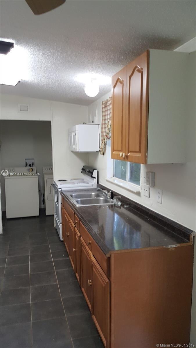 A kitchen features wooden cabinets, dark countertops, a double sink, and an adjacent laundry area — 19800 SW 180th Ave # 32, Miami FL 33187, MIAMI, FL