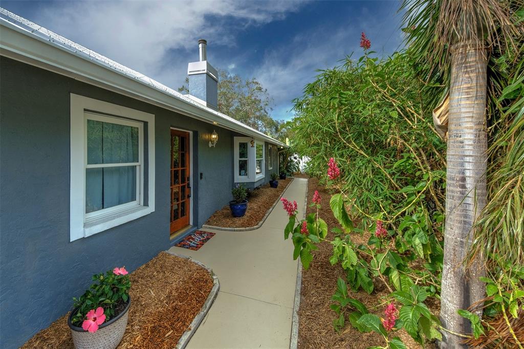 A gray house exterior with a concrete walkway, a wooden door, and lush landscaping — 2690 TEMPLE STREET, SARASOTA, FL