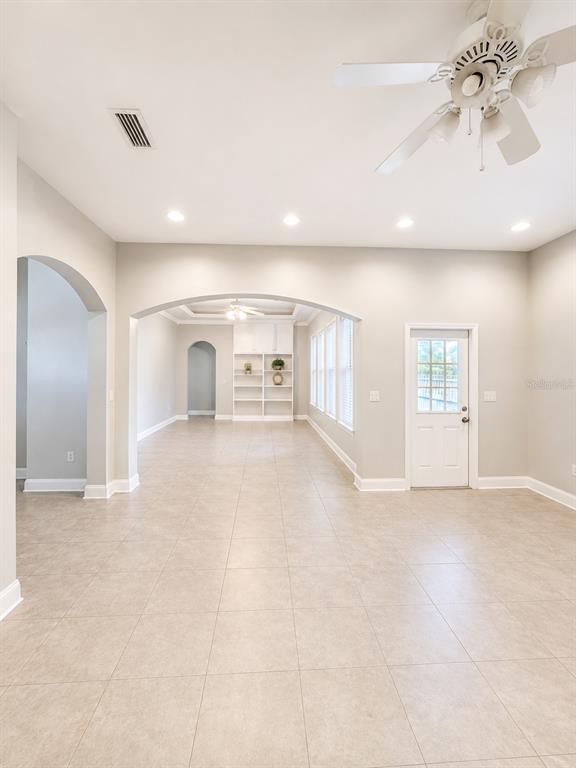 A spacious room with light tile flooring, arched entryways, a ceiling fan, and built-in shelving — 217 E 19TH AVENUE, MOUNT DORA, FL