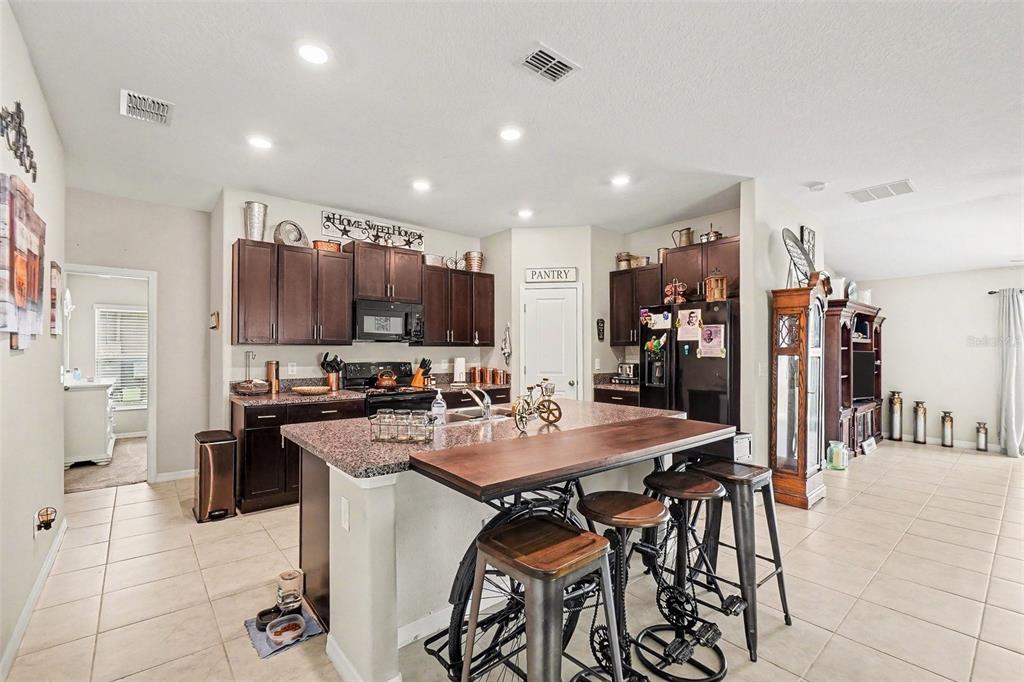 A kitchen features dark wood cabinets, granite countertops, and a unique bicycle-base island with stools — 14907 IMPERIAL PURPLE LANE, WIMAUMA, FL