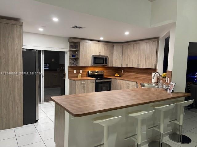 A kitchen features light wood cabinets, a wooden breakfast bar, and white tile flooring — 600 SE 25th Ln, Homestead FL 33033, HOMESTEAD, FL