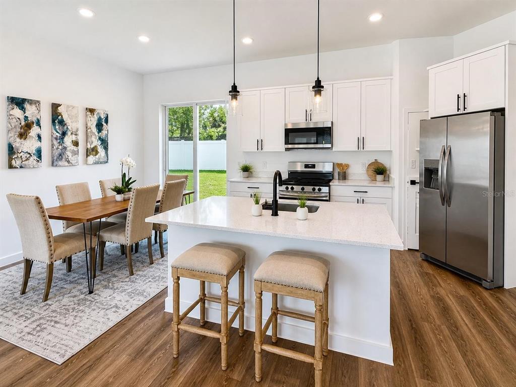 A modern kitchen features white cabinetry, stainless steel appliances, a quartz island, and dining area — 9509 N OLD MILL WAY, CITRUS SPRINGS, FL