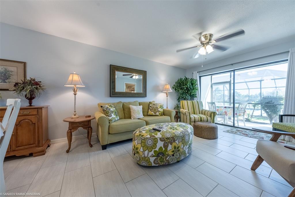 A living room features a green sofa, floral ottoman, tiled floors, and a sliding glass door — 1416 SAN CRISTOBAL AVENUE UNIT 3 (C), PUNTA GORDA, FL