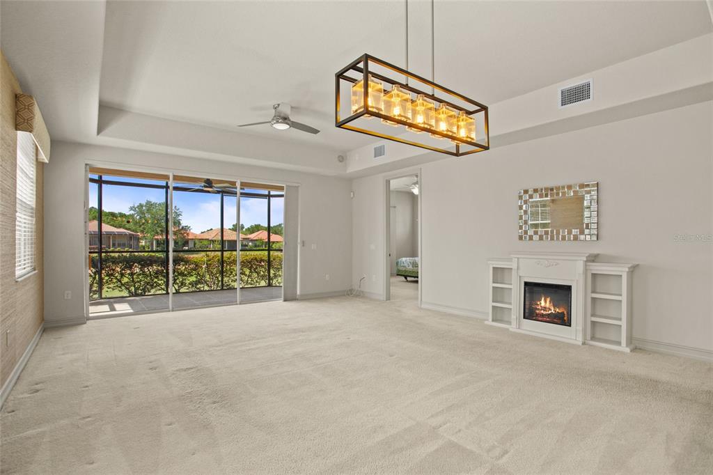 A living room with beige carpet, a fireplace, a rectangular chandelier, and sliding glass doors — 26207 AVENIDA LAS COLINAS, HOWEY IN THE HILLS, FL