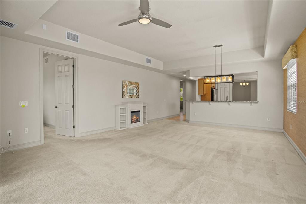 A spacious living room features beige carpeting, a ceiling fan, and a small electric fireplace — 26207 AVENIDA LAS COLINAS, HOWEY IN THE HILLS, FL