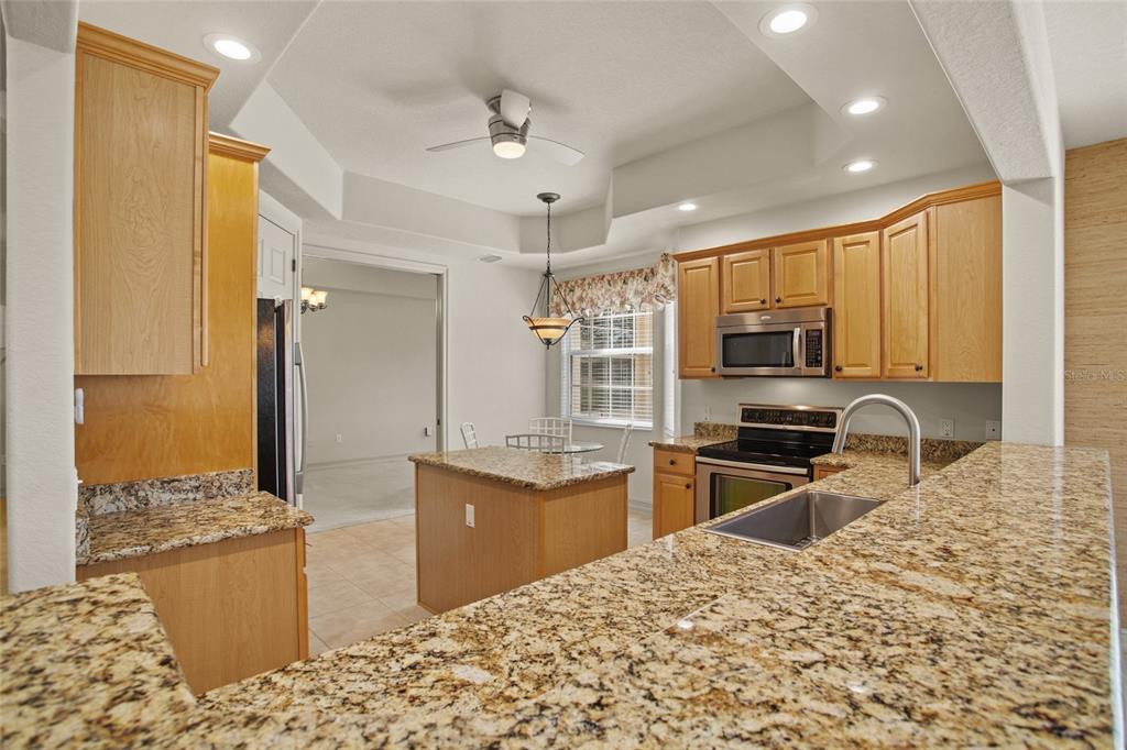 A kitchen with light wood cabinets, granite countertops, a center island, and stainless steel appliances — 26207 AVENIDA LAS COLINAS, HOWEY IN THE HILLS, FL