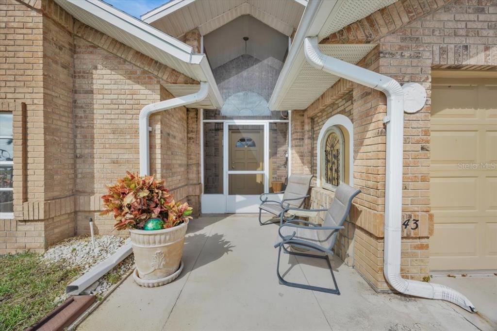 A brick house exterior features a covered entryway with two chairs and a potted plant — 543 CLUBHILL DRIVE, HAINES CITY, FL