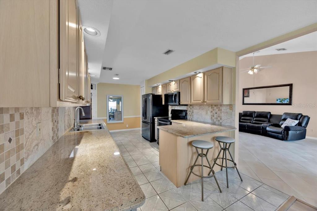 A kitchen with light wood cabinets, granite countertops, and a breakfast bar with two stools — 543 CLUBHILL DRIVE, HAINES CITY, FL