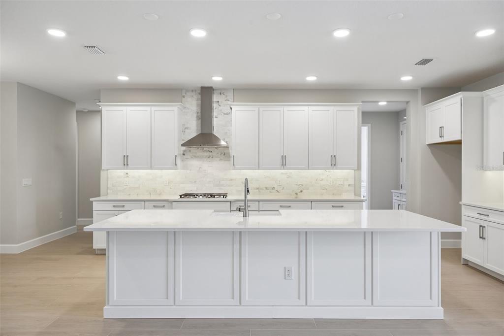 A modern kitchen features white cabinetry, a large central island with four stools, and stainless appliances — 3802 WOLVES CREEK PLACE, APOPKA, FL