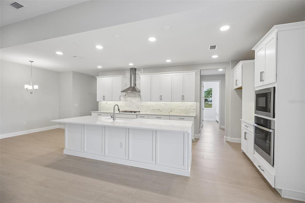 A dining room features a wooden table, woven chairs, arched windows, and light wood flooring — 3802 WOLVES CREEK PLACE, APOPKA, FL