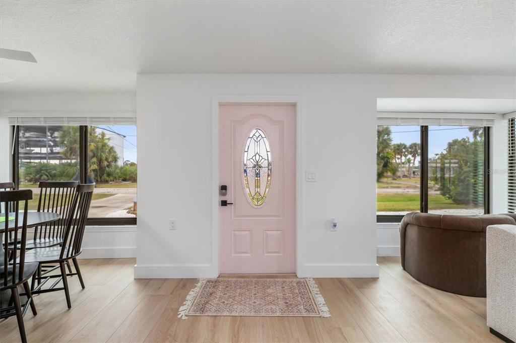 A light-filled room features a pink front door, light wood flooring, and large windows — 1950 NEBRASKA AVENUE, ENGLEWOOD, FL