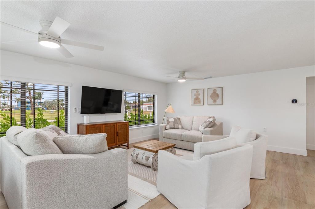 A bright living room features light-colored furniture, a television, and two ceiling fans — 1950 NEBRASKA AVENUE, ENGLEWOOD, FL