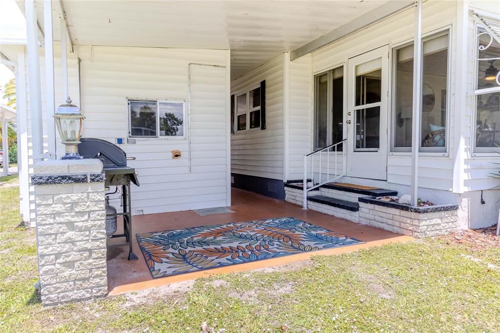 A covered patio with a grill, outdoor rug, and steps leading to a white house — 2100 KINGS HIGHWAY UNIT 336, PUNTA GORDA, FL