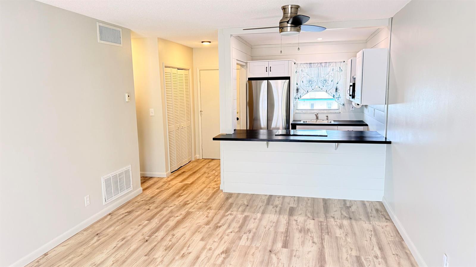 A kitchen with white cabinets and a dark countertop overlooks a living area with wood-look flooring — 1114 Lake Terrace # 205, Boynton Beach FL 33426, BOYNTON BEACH, FL