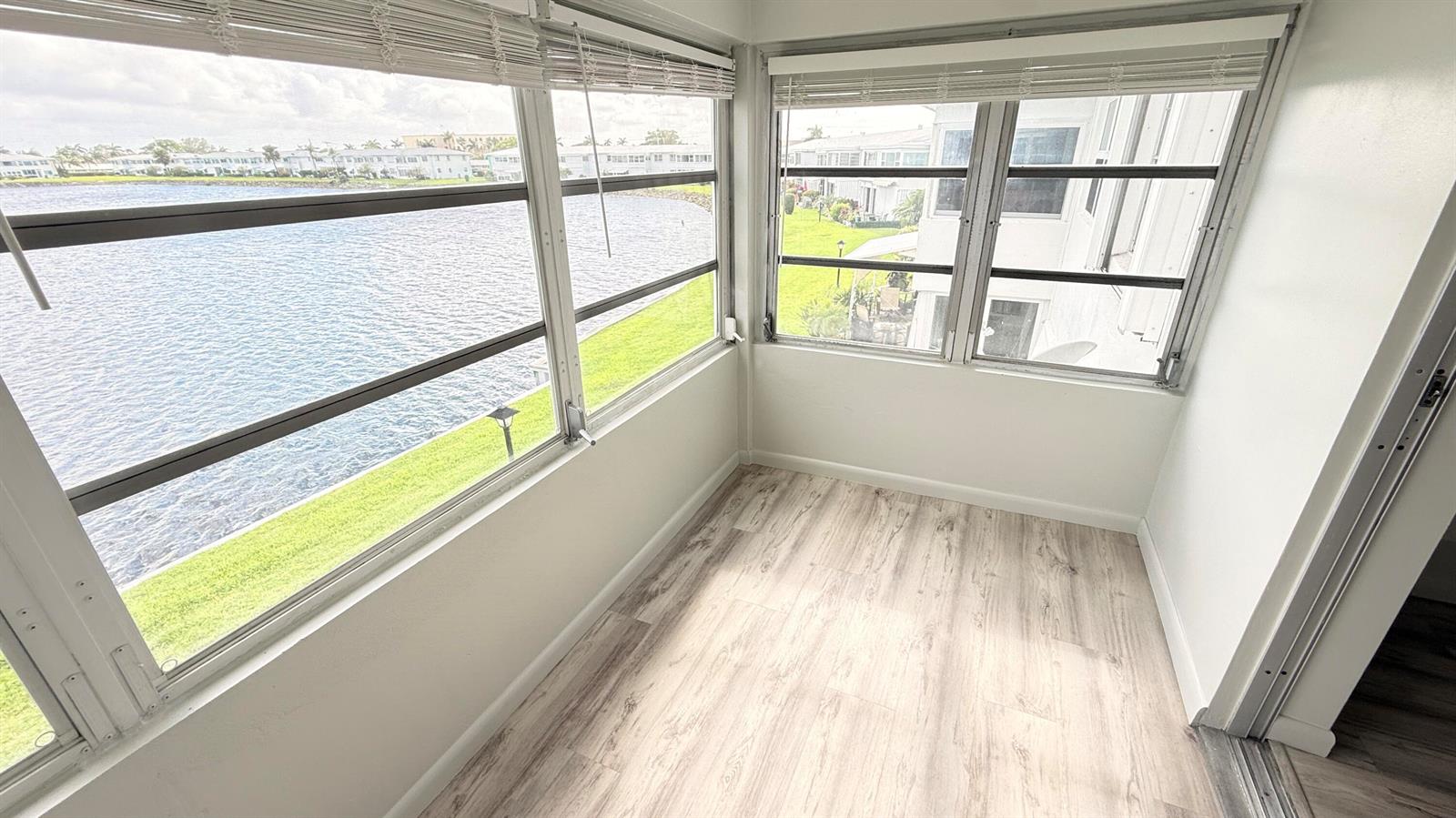 A sunroom with light wood-look flooring and large windows overlooking a lake and buildings — 1114 Lake Terrace # 205, Boynton Beach FL 33426, BOYNTON BEACH, FL