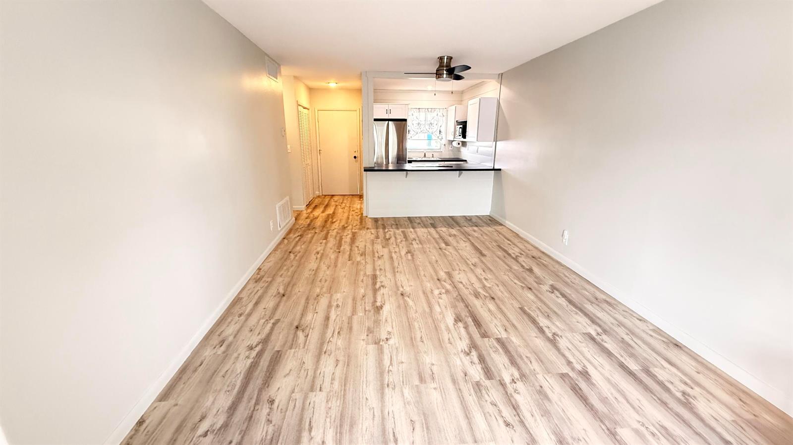 A living room with light wood-look flooring leads to an open kitchen with white cabinets — 1114 Lake Terrace # 205, Boynton Beach FL 33426, BOYNTON BEACH, FL
