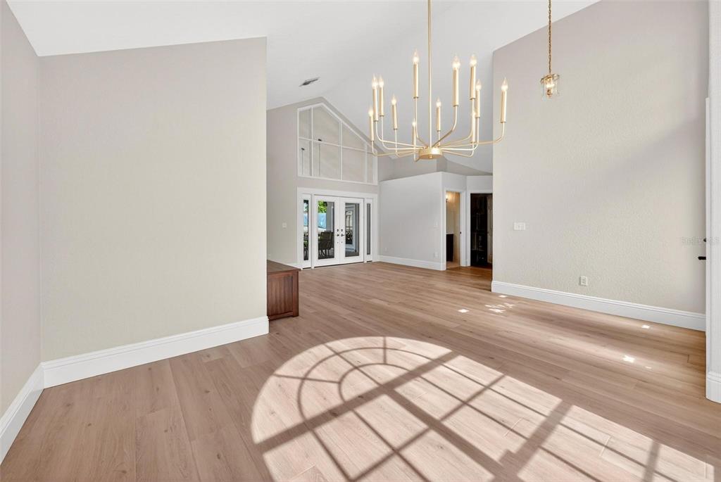 A bright, open-concept room features light wood flooring, a large chandelier, and vaulted ceilings — 2800 CONWAY GARDENS ROAD, ORLANDO, FL