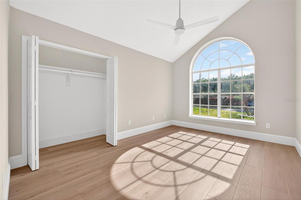 An empty bedroom features light wood flooring, a vaulted ceiling, a ceiling fan, and arched windows — 2800 CONWAY GARDENS ROAD, ORLANDO, FL